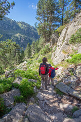 mother and son walk down a mountain trail hand in hand with backpacks and mountain clothing, vertical