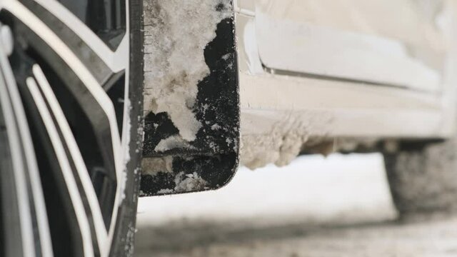 man knocks down accumulated snow from fender liner in winter. Cleaning car after the road from snow and mud.