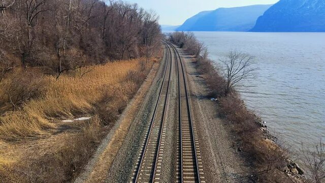 Aerial Drone Footage Down Railroad Train Tracks In A River Valley With Mountains And Water In Early Spring. This Is The Amtrak Hudson Line In New York In The Hudson Valley