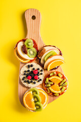 Crispy puffed rice cakes on board with fresh fruit kiwi banana apple blueberries raspberries and orange on the yellow background - top view on healthy organic vegetarian or vegan breakfast gluten free
