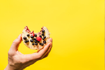 Hand holding crispy puffed rice cake with fresh fruit blueberries raspberries in front of the the yellow background - healthy organic vegetarian or vegan breakfast gluten free copy space