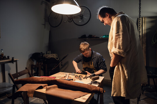 an experienced shoemaker and his assistant in their workshop make shoes from leather to order