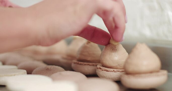Close up of female hands putting hazelnuts on ganache cream on caramel macarons shells on the table. Macaroon Baking Concept. Cooking, Food And Baking Concept. Confectionery And Baking Concept