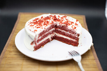 Red velvet cake, classic three layered cake from red butter sponge cakes with cream cheese frosting, American cuisine, white plate, bamboo coat