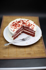 Red velvet cake, classic three layered cake from red butter sponge cakes with cream cheese frosting, American cuisine, white plate, bamboo coat