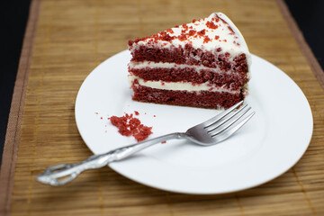 Red Velvet cake slice on wooden table, bamboo coat, white plate