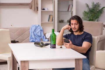 Young unemployed man drinking alcohol at home