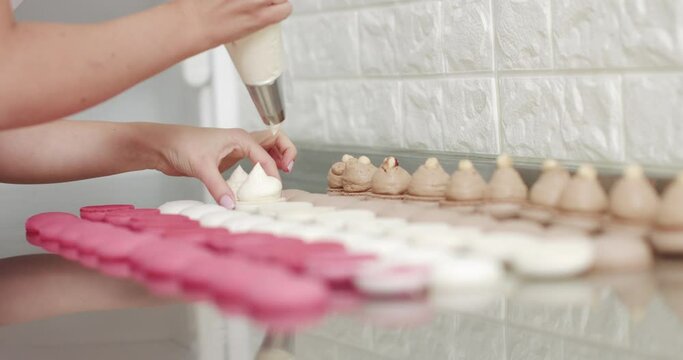 Cooking, Food And Baking Concept - Confectionery Bag Or Injector Squeezing Cream Filling To Macarons Shells At Pastry Shop. Chef With Confectionery Bag Squeezing Cream Filling To Macarons Shells