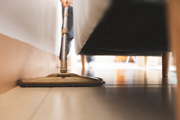 Asian woman cleaning and mopping the floor under the sofa with a microfiber wet mop pad in the...