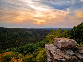 Fototapeta premium Overlook of the mountains and the fall foliage at Coopers Rock State Forest in West Virginia with the sunset golden sky one direction and a blue swirly sky the other direction, with the rock cliff.