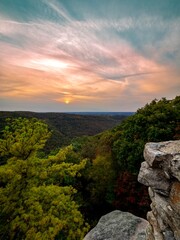 Overlook of the mountains and the fall foliage at Coopers Rock State Forest in West Virginia with the sunset golden sky one direction and a blue swirly sky the other direction, with the rock cliff.