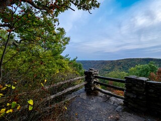 Fototapeta na wymiar Overlook of the mountains and the fall foliage at Coopers Rock State Forest in West Virginia with the sunset golden sky one direction and a blue swirly sky the other direction, with the rock cliff.