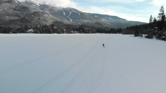 Aerial drone footage of cross country skier on frozen winter lake in Whistler, BC. 4K 24FPS.