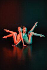 Two young gymnasts in a pose on a black background with neon lighting mixed light.