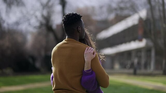 Interracial couple embrace outside. Young woman hugs partner