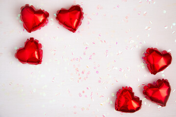 Heart-shaped foil balloons and shiny confetti on a light background. Valentine's day holiday concept. Flat lay.