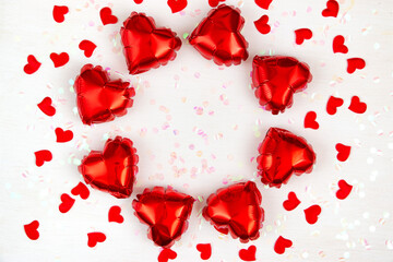 Heart-shaped foil balloons and shiny confetti on a light background. Valentine's day holiday concept. Flat lay.