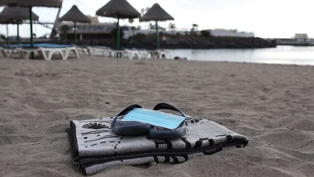 Surgical mask on flip flops and a towel on the beach, new normality on the beach, social distancing and protective mask