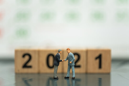 2021 New Year Global Business Concept. Two businessman miniature figure people make a hand shake with wooden number block and calendar as background. - Powered by Adobe