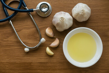 Top view of garlic ,garlic oil and stethoscope on wooden background.