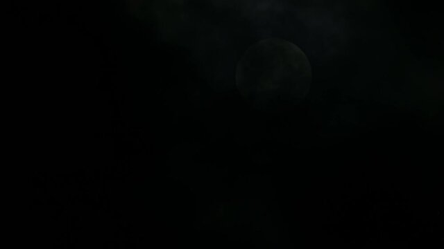 Moon almost seen behind the dark clouds in the middle of the night; slowly revealed as dark clouds move down the frame, one cold winter night at Kaeng Krachan National Park, Thailand.