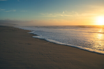 Beach sunset. Empty sand beach, sea waves, and sun setting down the horizon. Tranquil, calm scene, soft focus, copy space