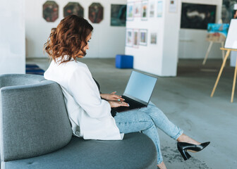 Charming young woman businesswoman designer in white suit using laptop in the modern art gallery