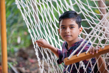 Indian Little boy resting in hammock on garden