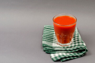 A full glass of tomato juice and a green checkered napkin on a g