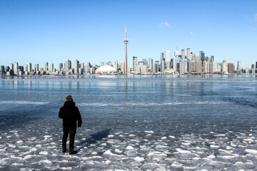 Man walking on frozen lake with city skyline in background on sunny day