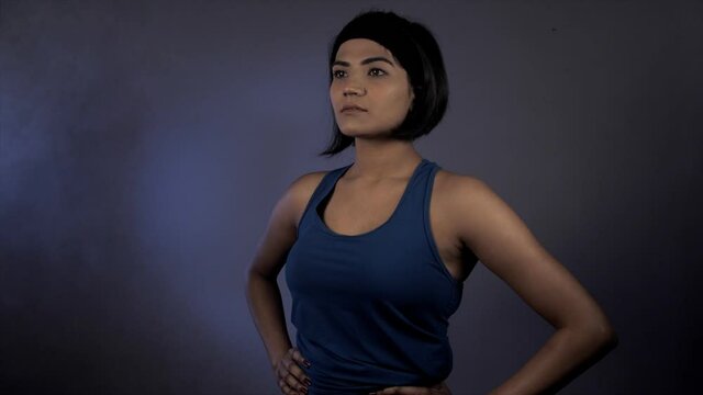 Portrait of a gymnast in blue clothes staring away from the camera - Indian athlete . Medium shot of a confident young sportswoman standing alone against a dark background - active healthy lifestyle