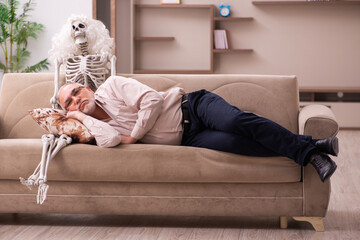 Old man sitting on the sofa with the female skeleton