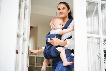 Pretty young mixed-race woman opening entrance door and leaving house with baby boy in carrier