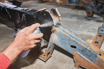 Car Mechanic or Auto Mechanic Spray Black Paint Side of Car Chassis in Garage