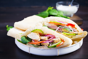 Pita stuffed with chicken, tomato, cucumber and spinach on wooden background. Middle Eastern cuisine.
