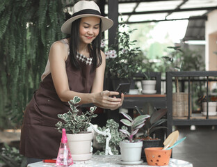Asian female gardener wearing hat and apron working in her home  garden, taking photo  of her ...