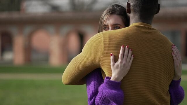 Interracial couple embrace outside. Young woman hugs partner