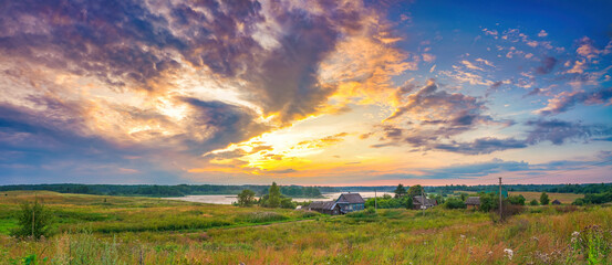 Panoramic view on bright sunset over lake and old village in countryside