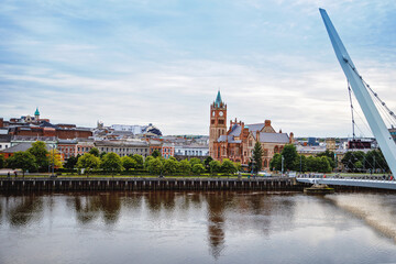 Derry, Ireland. Illuminated Peace bridge in Derry Londonderry, City of Culture, in Northern Ireland with city center at the background. Night cloudy sky with reflection in the river at the dusk