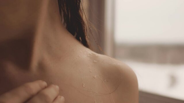 Slowly, with the fingers of her hand, the woman touches the drops of water on her bare shoulder. The collarbone protrudes beautifully on the neck. Loose wet hair at the back of the neck. close-up.