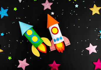 Two space rockets made of colored paper on a black background with colored stars. The concept of crafts by the day of April 12 human space flight.