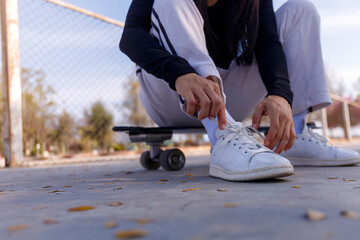 Young women sitting on a surf skate board tying a shoe before play. Young girl long hair sitting and tying a sneaker at public park on morning before play surf skate board