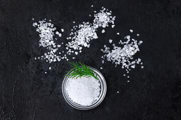Coarse salt crystals on a black table. Bowl with sea salt. Background for advertising salty.
