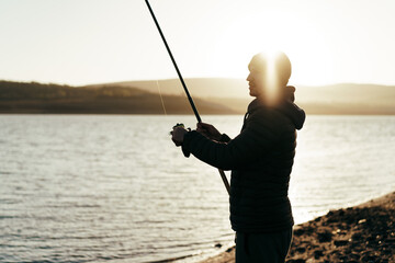 Young fisherman standing on the shore of lake with fishing rod
