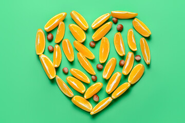 Heart made of cut oranges and hazelnuts on color background