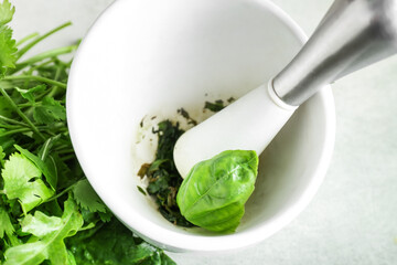 Mortar with herbs and pestle on light background