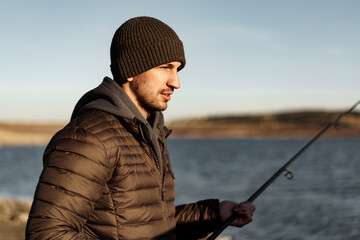 Young fisherman standing on the shore of lake with fishing rod
