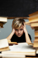 Sad boy sits at a table with books. Depression, loneliness, learning difficulties. Vertical.