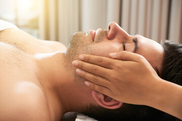Calm handsome young man enjoying relaxing and rejuvenating face massage in beauty salon