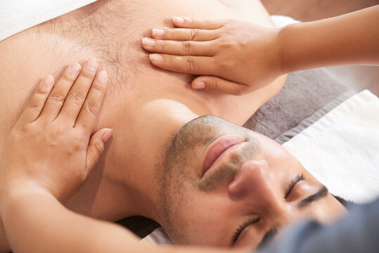 Close-up image of masseuse massaging chest and shoulders of young calm man in spa salon